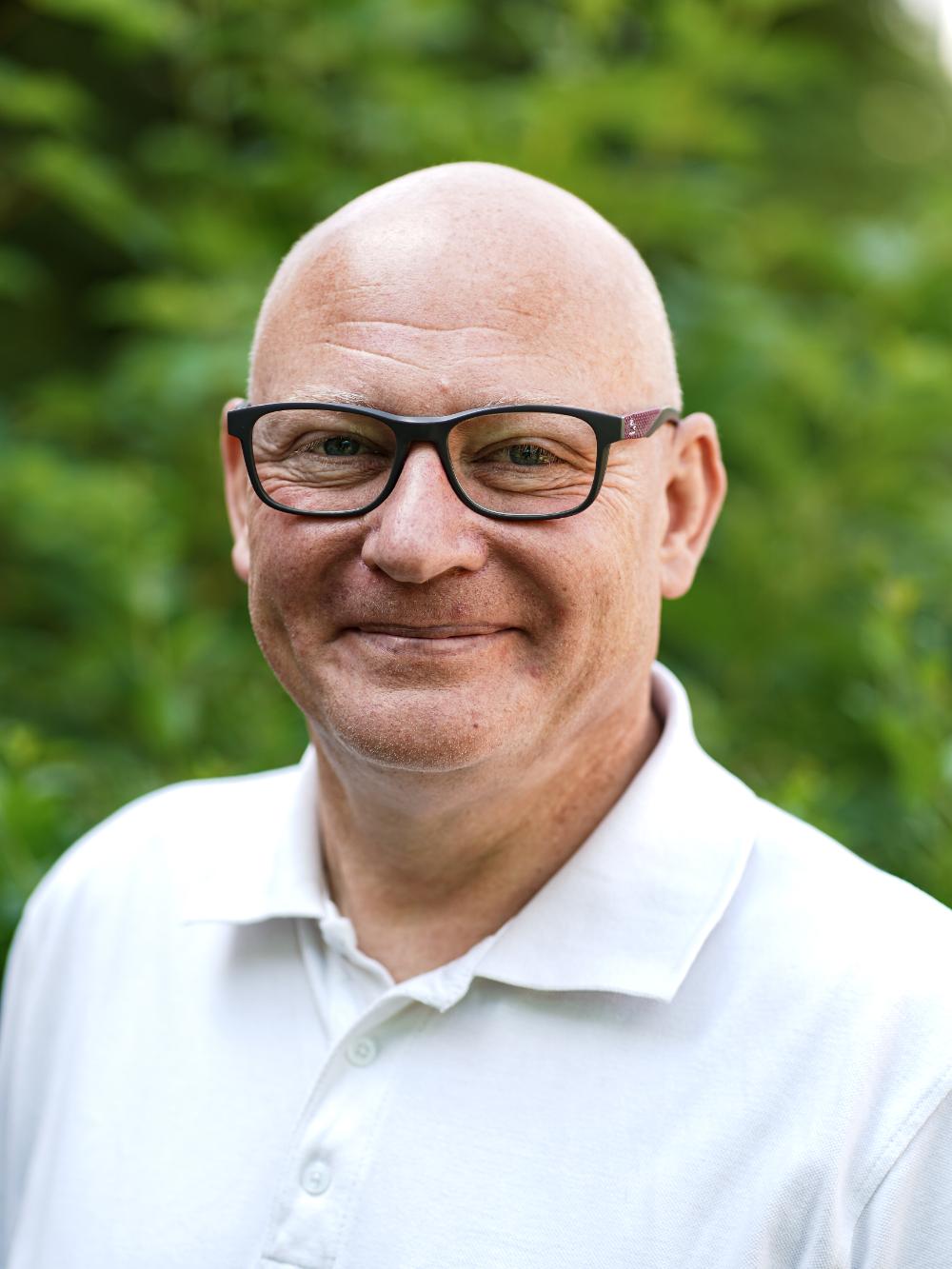 Mann mit Glatze, Brille und weißem Hemd.
