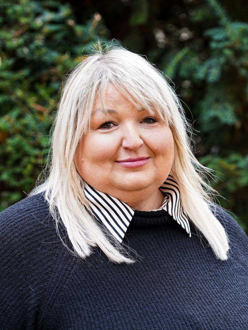Frau mit blondem Haar und schwarzem Oberteil. 