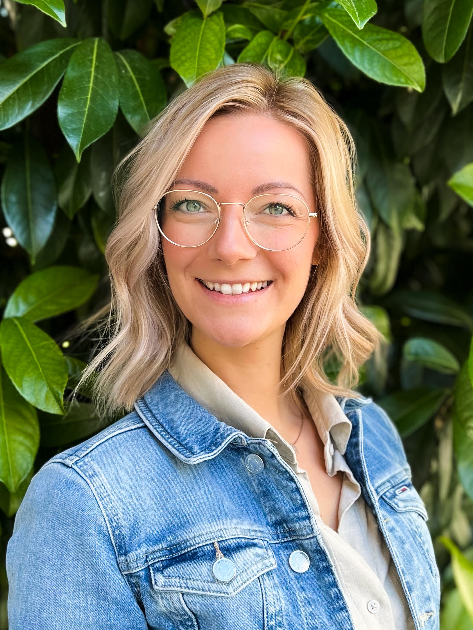 Blonde Frau mit Brille und Jeansjacke.